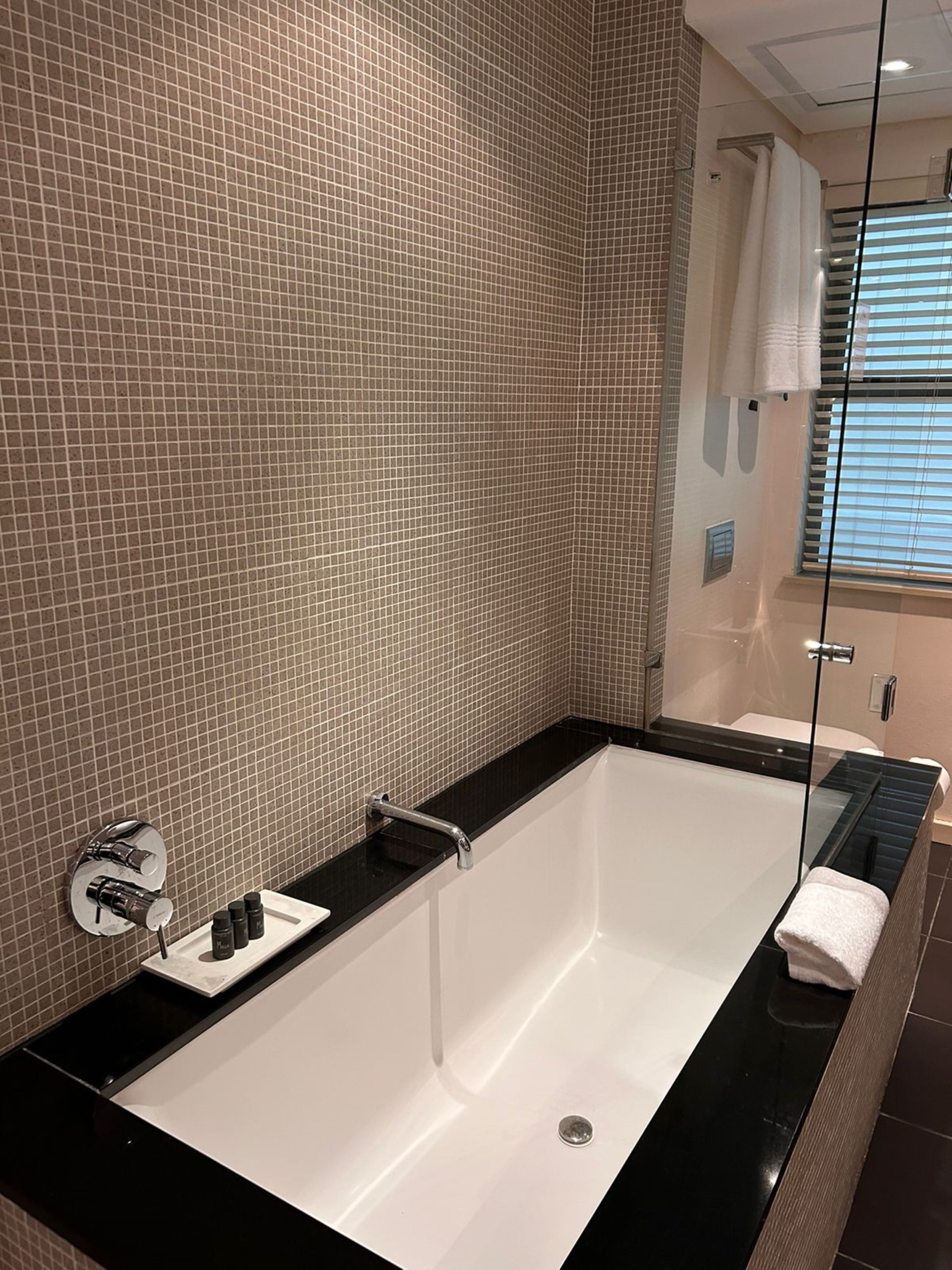 A modern bathroom with a large bathtub, a glass shower enclosure, and a tiled wall.