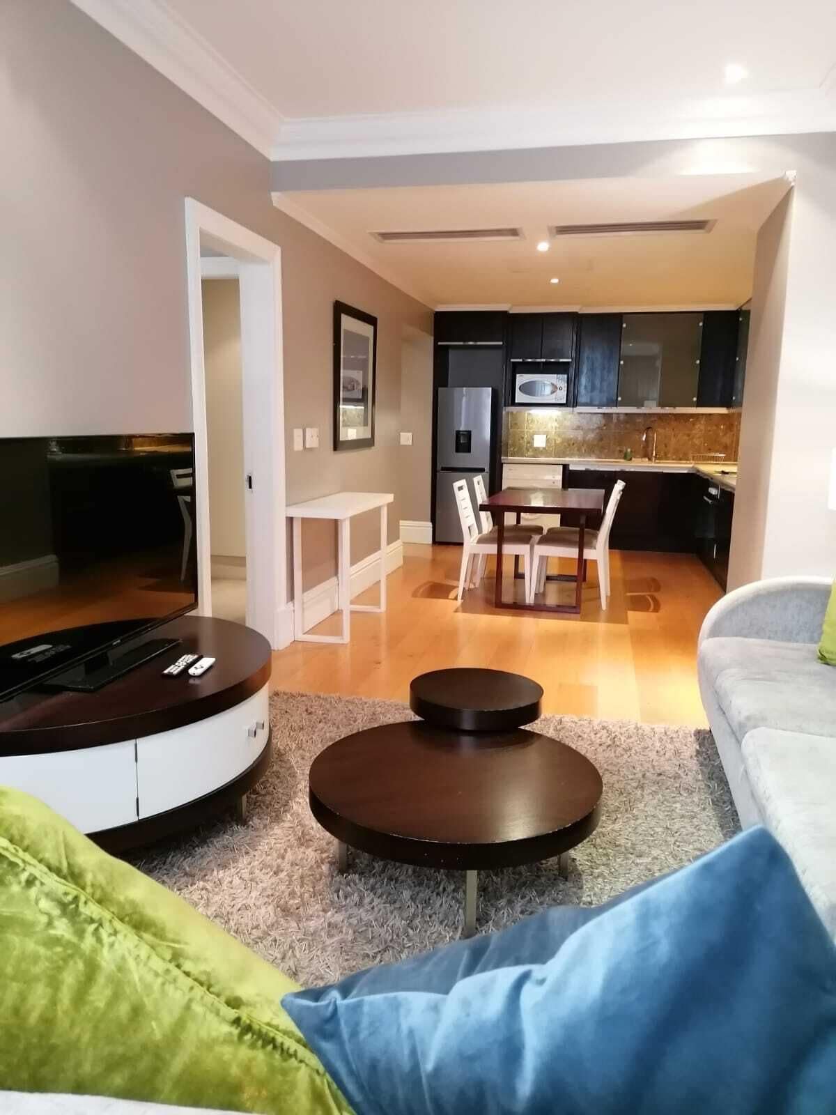 A modern living room with a TV, a dining area with chairs, a kitchen with cabinets, and a sofa.