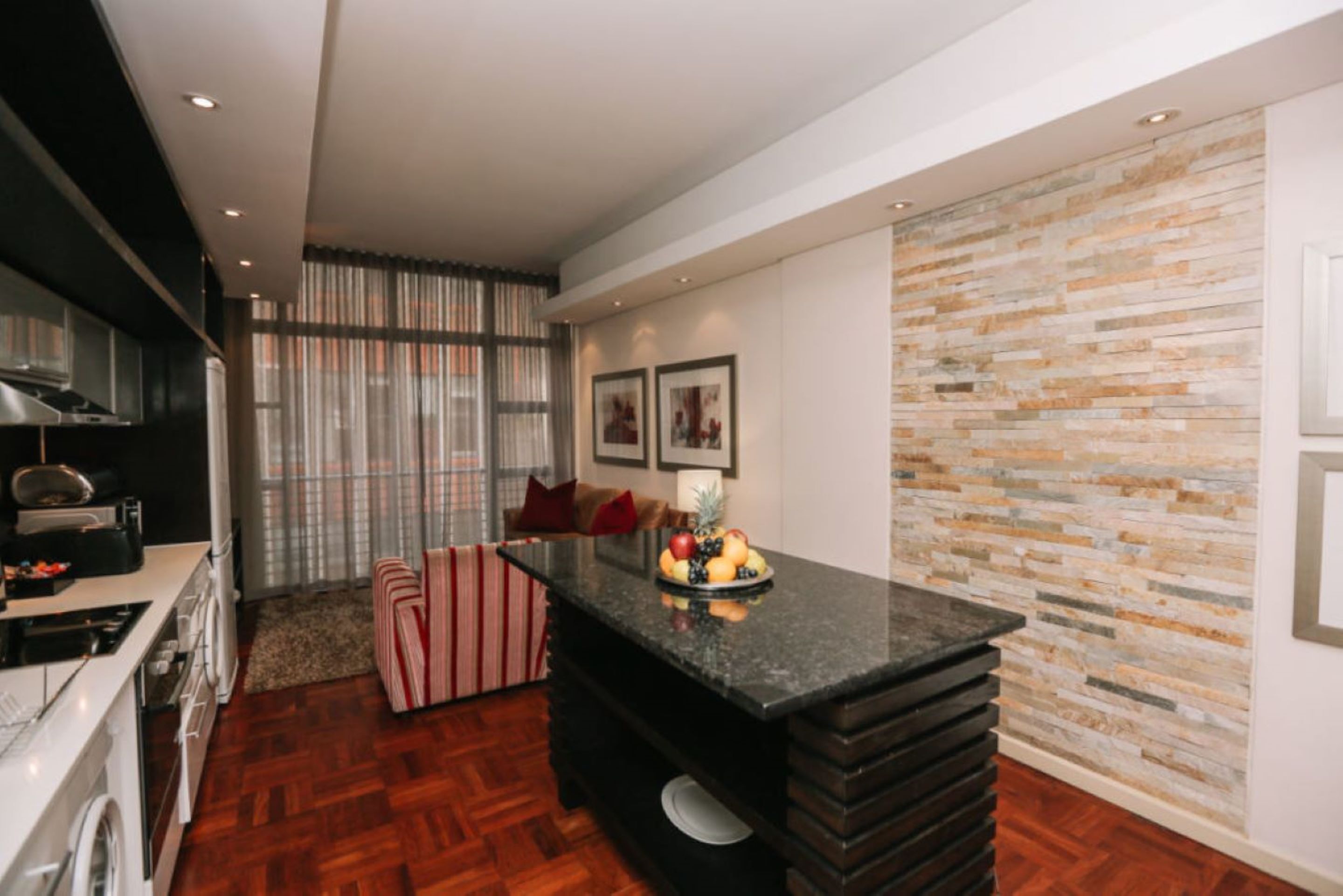 A modern kitchen with a central island, a dining area with striped chairs, and a stone accent wall.