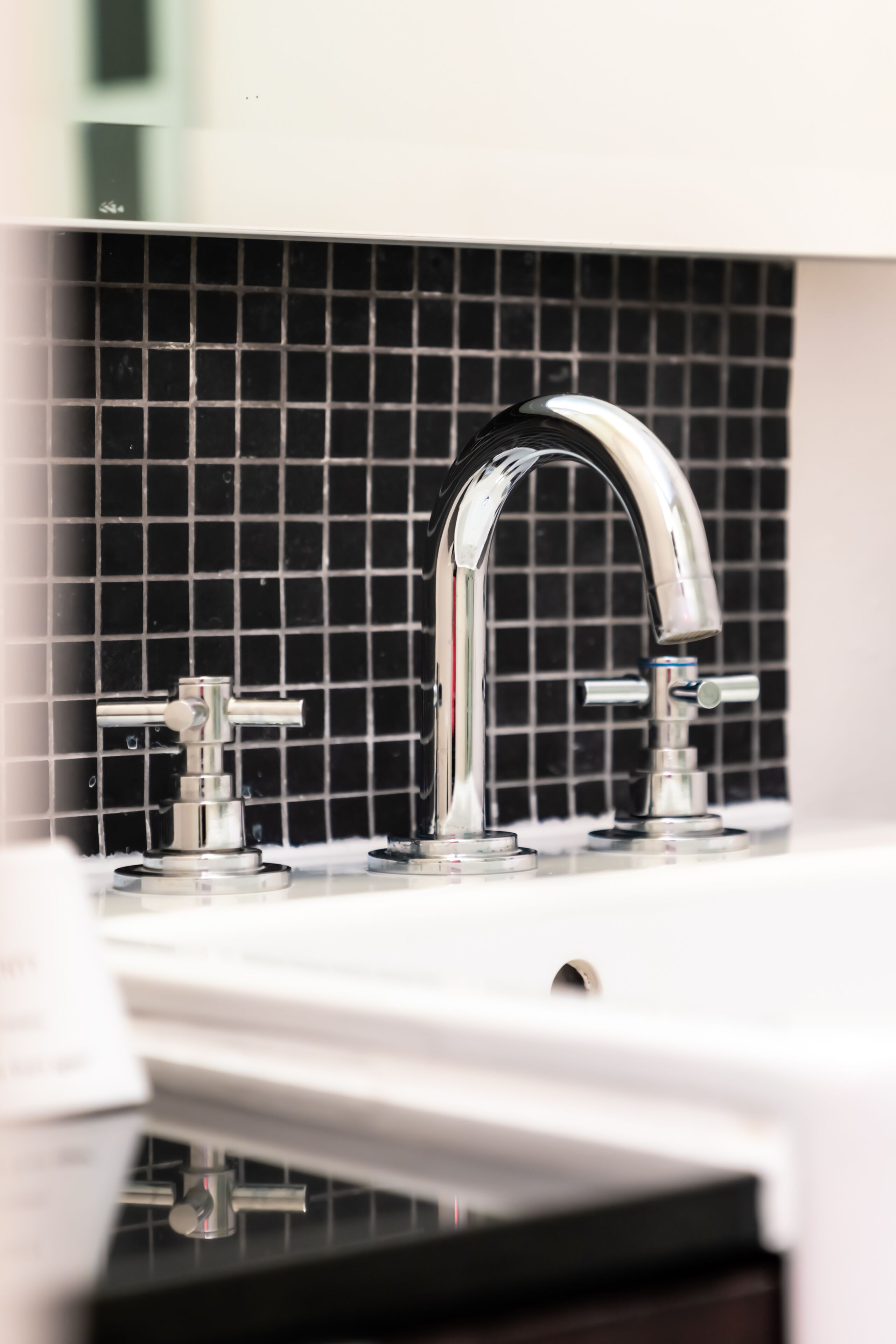 A modern bathroom with a chrome faucet and a black tiled backsplash.