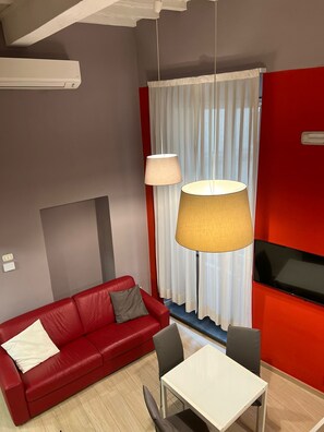 Ein modernes Wohnzimmer mit einem roten Sofa, zwei Sesseln, einem weißen Tisch und einem großen Fenster mit Vorhängen.