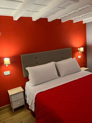 Ein Schlafzimmer mit roter Wand, grauem Kopfteil, weißer Bettwäsche, zwei Nachttischlampen und einem kleinen Nachttisch.