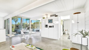 A modern kitchen with white cabinets, a dining area with a white table and chairs, and a large sliding glass door leading to an outdoor patio. - 1957 Modern Hideaway - A Ryson Property (Palm Springs)