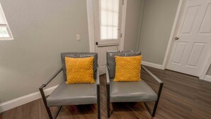 A room with two grey chairs with black metal legs and yellow cushions, a white door, and a window with blinds. - Lemon Drop Lane condo on Table Rock Lake! (Branson)