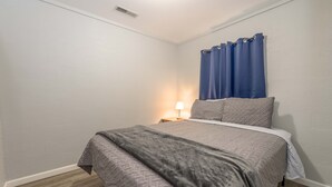 A bedroom with a bed, a nightstand, a lamp, and blue curtains. - Lemon Drop Lane condo on Table Rock Lake! (Branson)