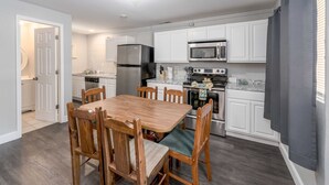 A modern kitchen with white cabinets, stainless steel appliances, and a wooden dining table with chairs. - Lemon Drop Lane condo on Table Rock Lake! (Branson)