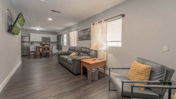 A modern living room with a grey sofa, a wooden coffee table, and a grey armchair. A kitchen is visible in the background with white cabinets and a microwave. - Lemon Drop Lane condo on Table Rock Lake! (Branson)