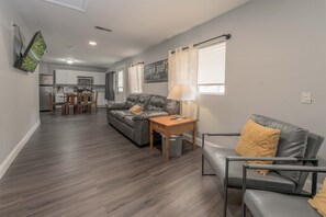 A modern living room with a grey sofa, a wooden coffee table, and a grey armchair. A kitchen is visible in the background with white cabinets and a microwave. - Lemon Drop Lane condo on Table Rock Lake! (Branson)