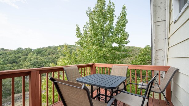 A wooden deck with a table and chairs, overlooking a forested hillside. - A-Frame Cabin on Table Rock Lake, by SDC! (Branson)