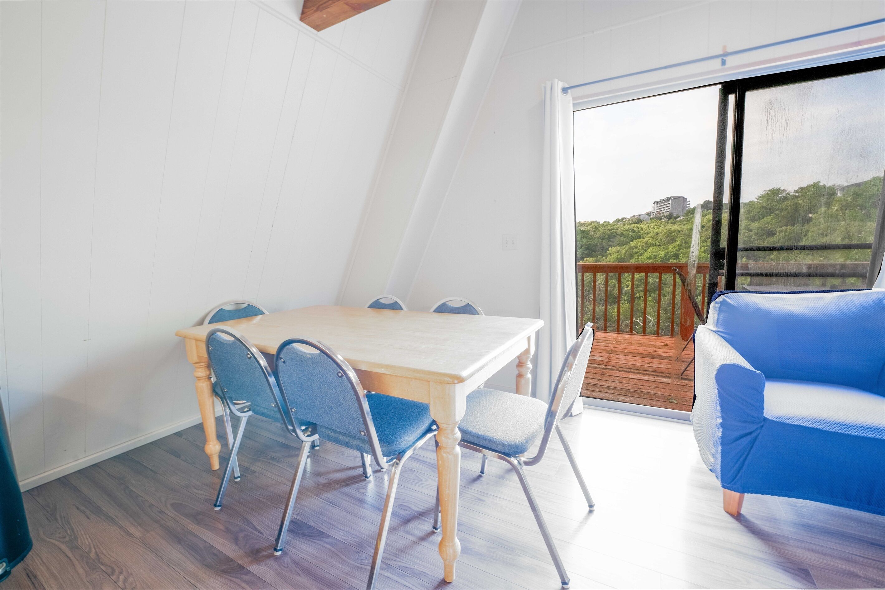 A dining area with a wooden table and chairs, a blue sofa, and a view of greenery through a glass door.