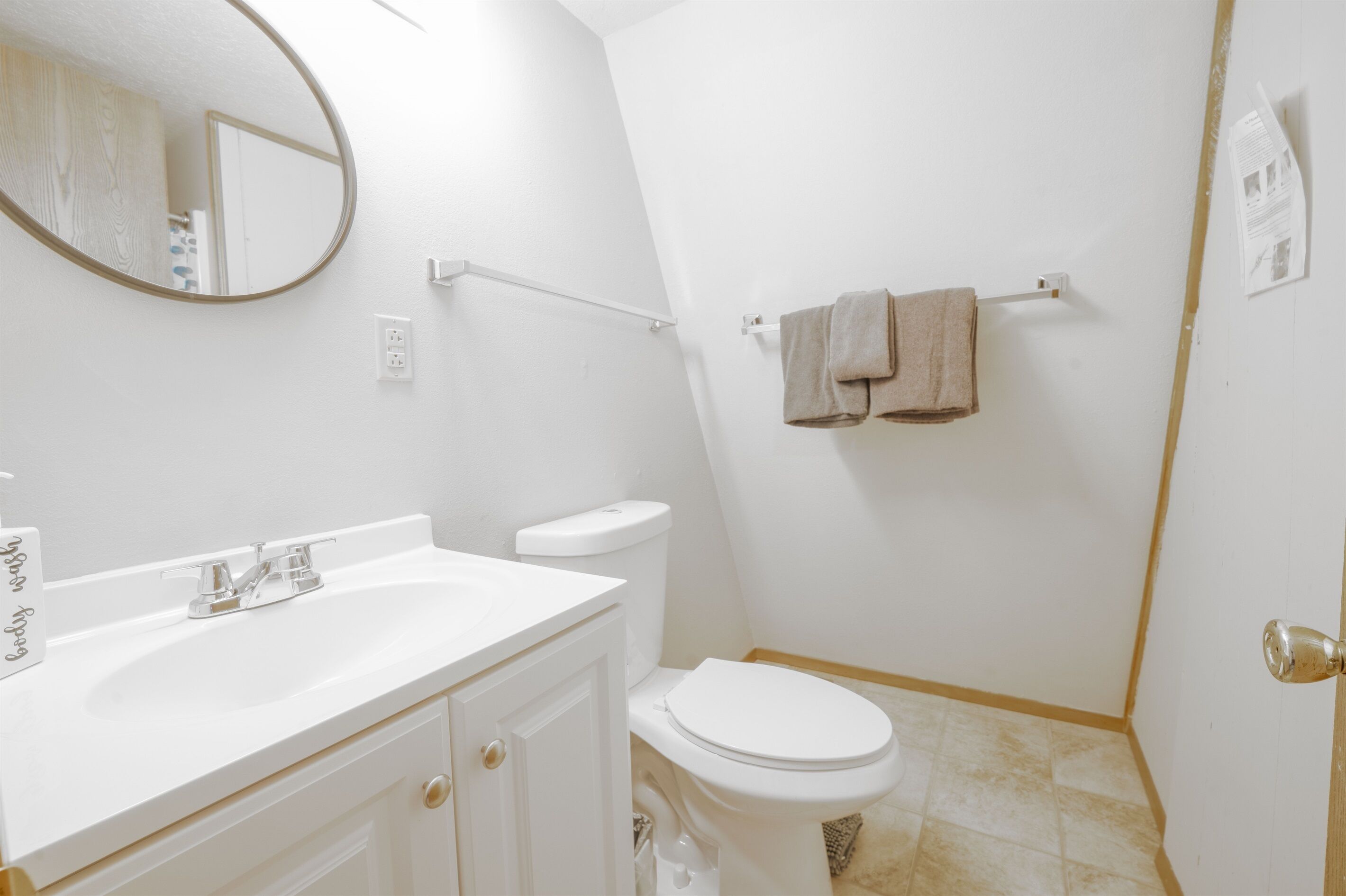 Un baño con lavamanos blanco, espejo, inodoro y toallero.