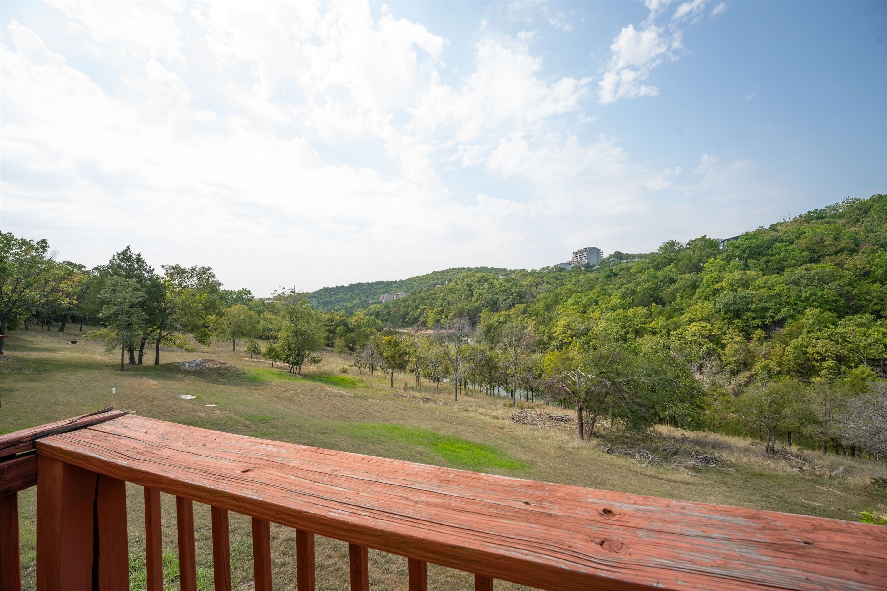 Una terraza de madera con vistas a un área verde con árboles y una colina al fondo.