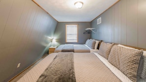 Quarto com duas camas, janela com persianas, luminária pendente e aquecedor fixado na parede.