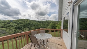 Um terraço com mesa e cadeiras, com vista para uma encosta arborizada.