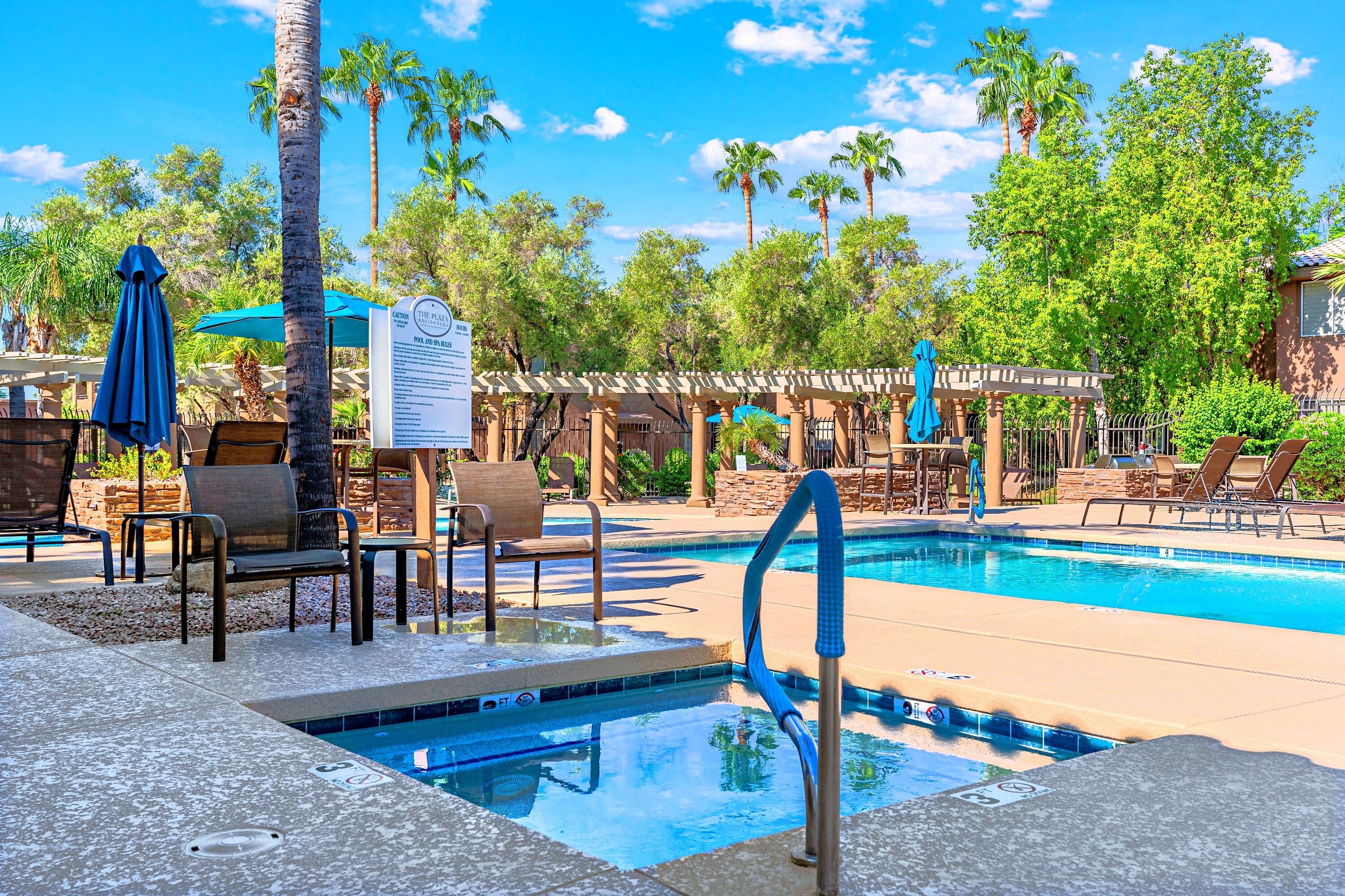 A pool area with lounge chairs, a hot tub, and a pergola.