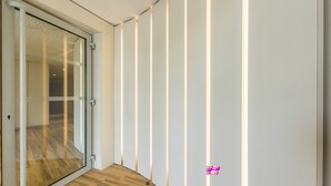 Un interno moderno con una porta vetrata che conduce in una stanza, pavimento in legno e strisce di luce verticali sulla parete.