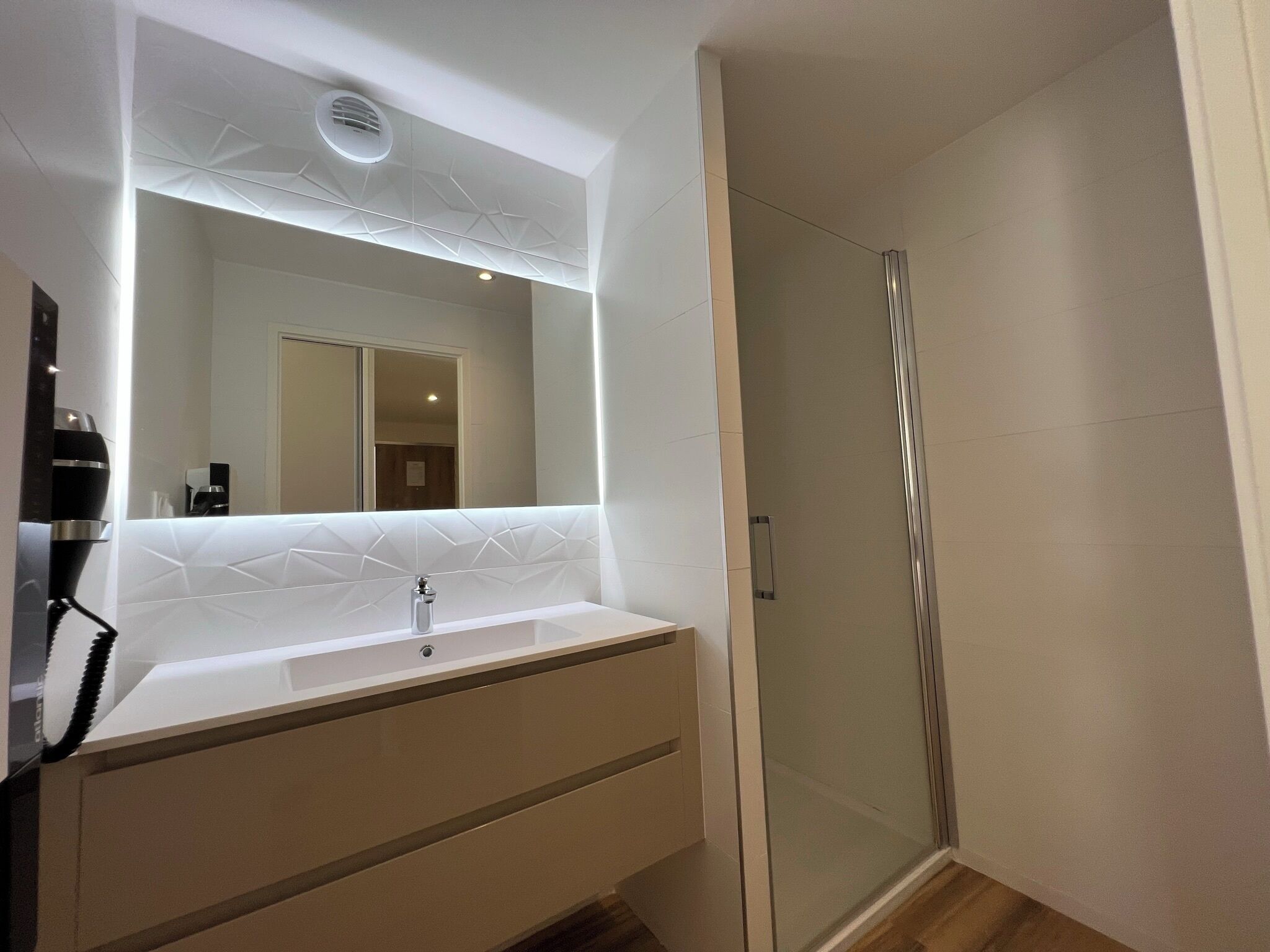 A modern bathroom with a large mirror, a sink, and a glass-enclosed shower.