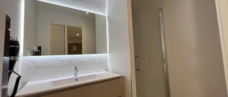 A modern bathroom with a large mirror, a sink, and a glass-enclosed shower.