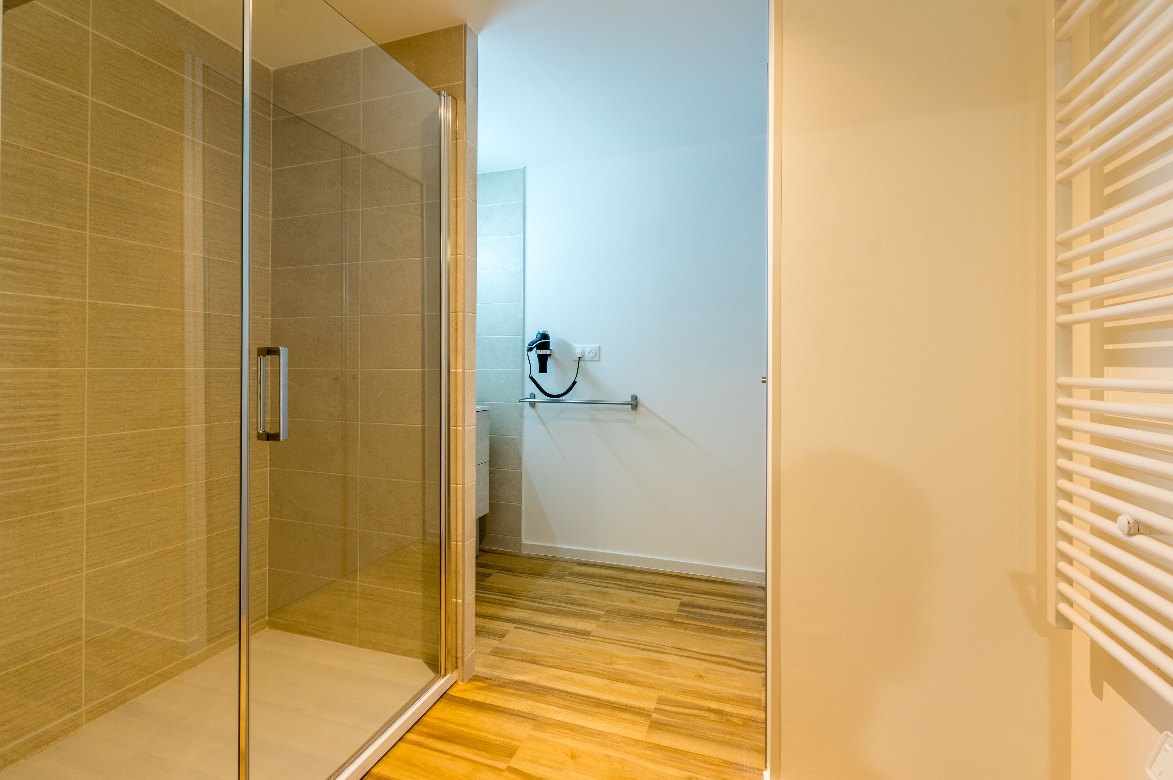 Un baño moderno con cabina de ducha de vidrio, pared de azulejos blancos y suelo de madera.