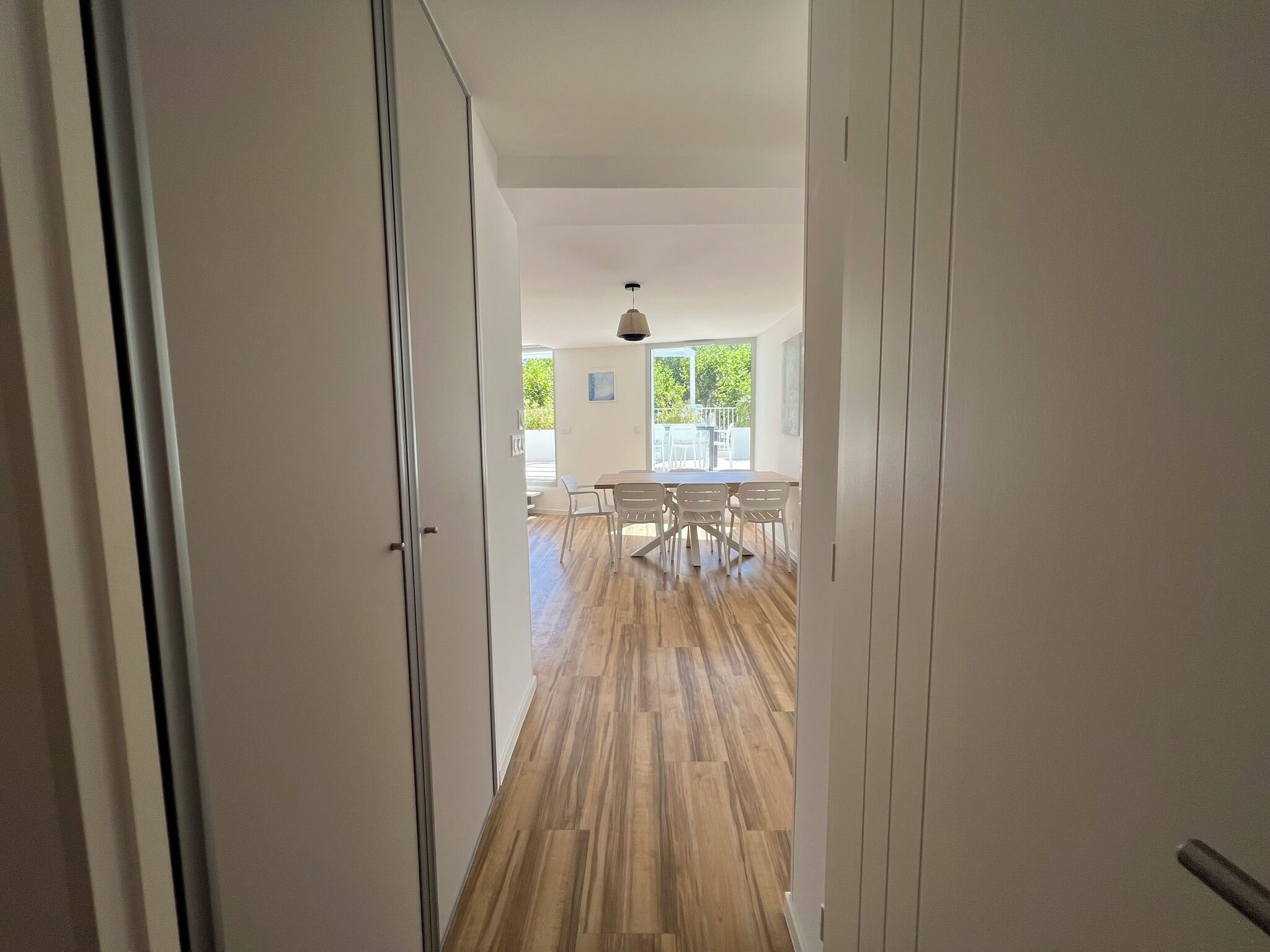 A hallway with wooden flooring leading to a dining area with a table and chairs.