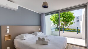 Camera d'albergo moderna con un letto grande, una testiera in legno, un comodino e vista su un balcone con un albero e ringhiera.