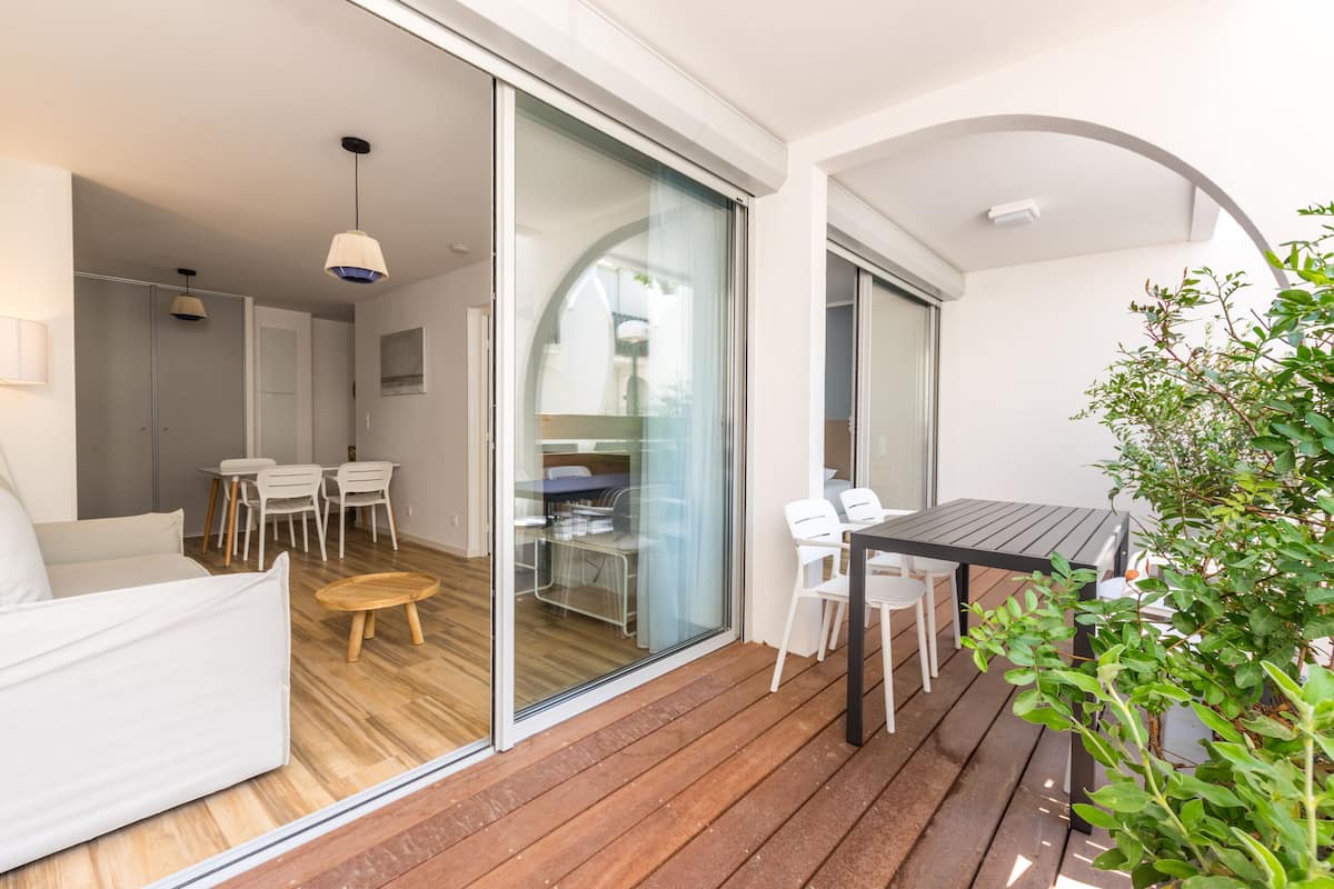 A modern living room with a sofa, a small round table, and a glass door leading to a dining area with a table and chairs.