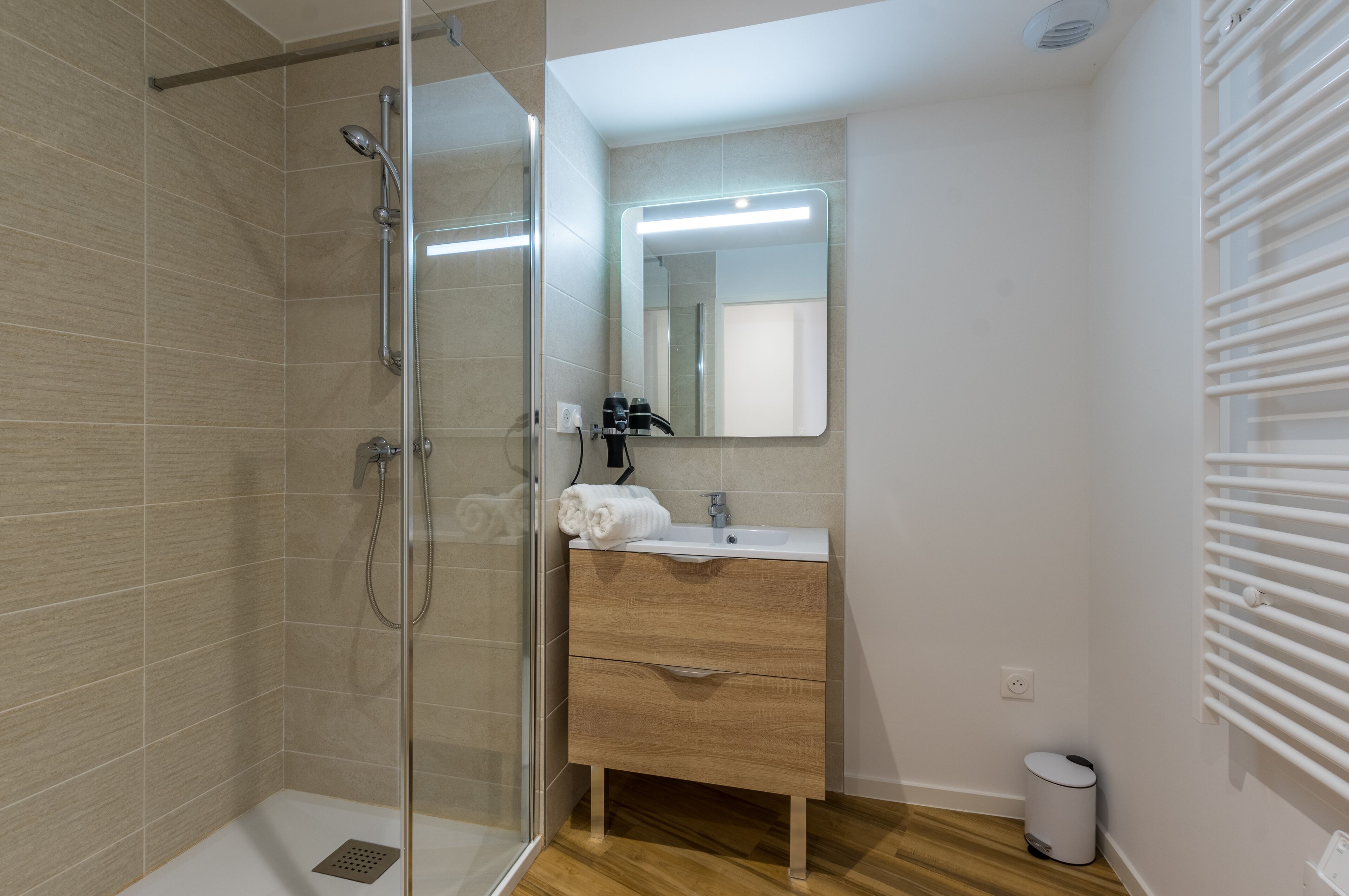 A modern bathroom with a glass-enclosed shower, a wooden vanity with a mirror, and a white sink.