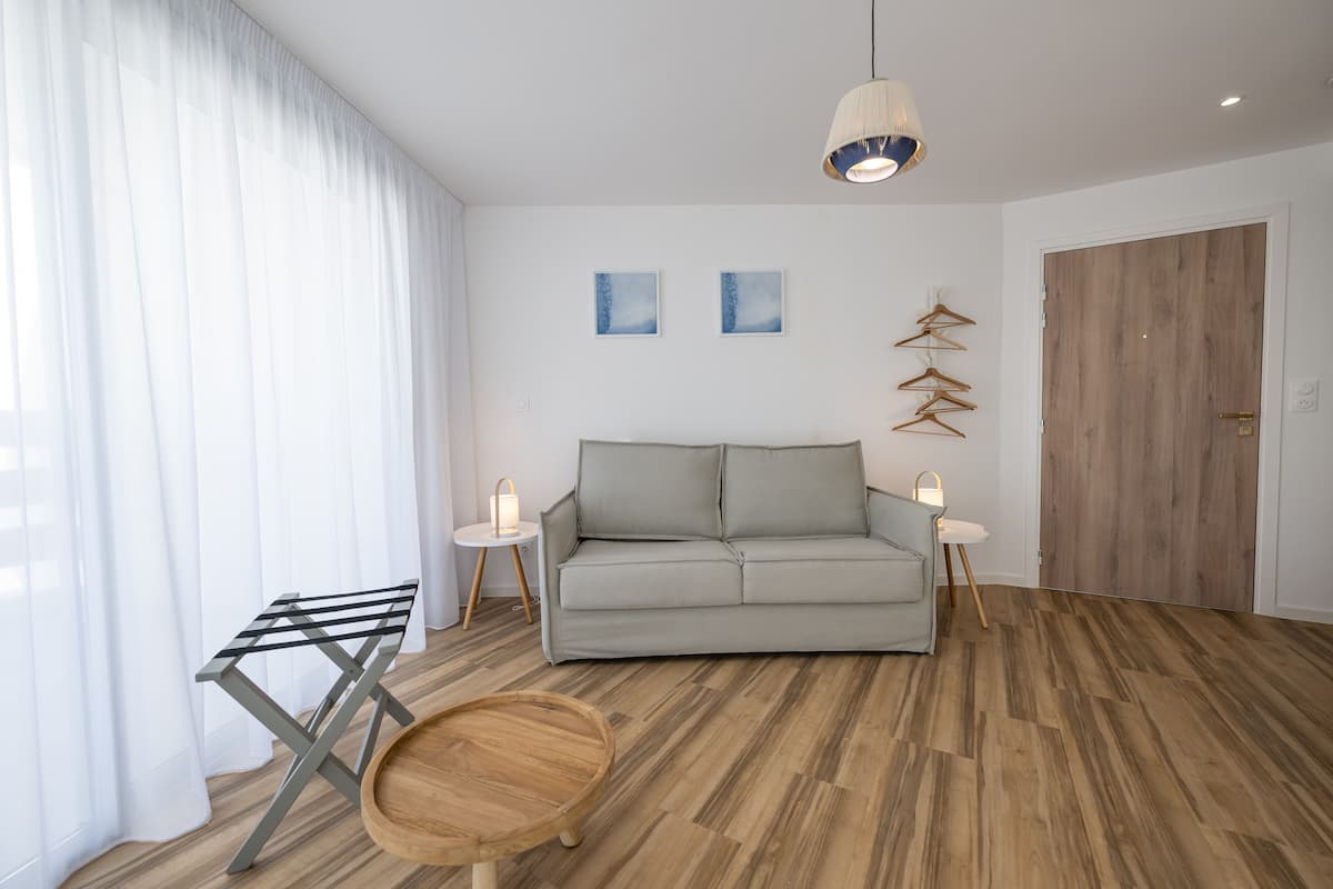 A modern living room with a grey sofa, wooden flooring, a hanging light fixture, and a door with a wooden finish.