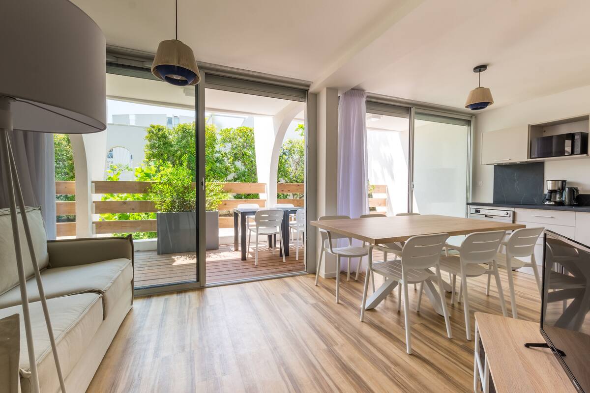 A modern kitchen with a dining area, large sliding glass doors to a deck, and a sofa.