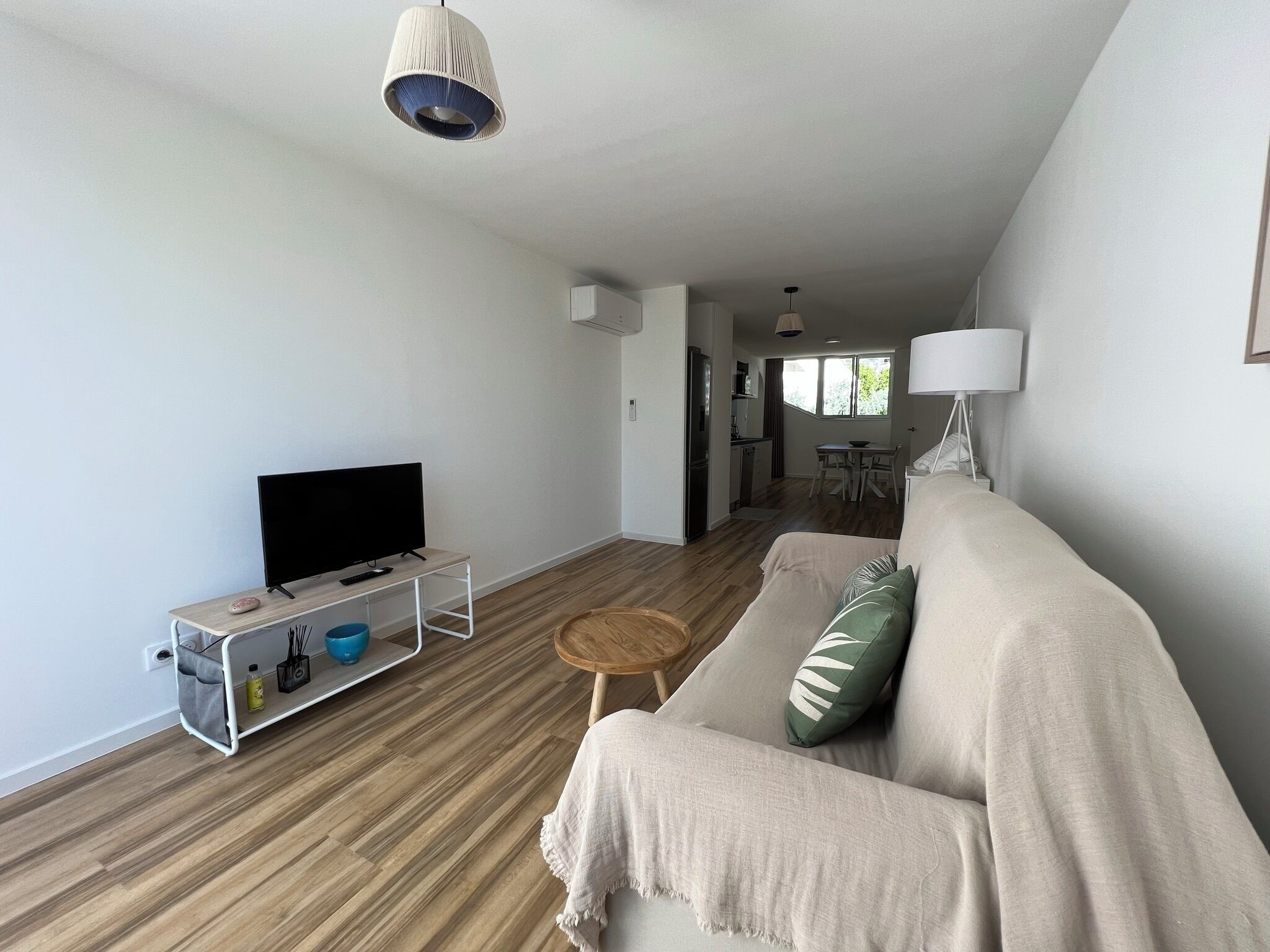 Een woonkamer met een bank, een televisie op een dressoir, een klein rond tafeltje, en een keuken in de achtergrond.
