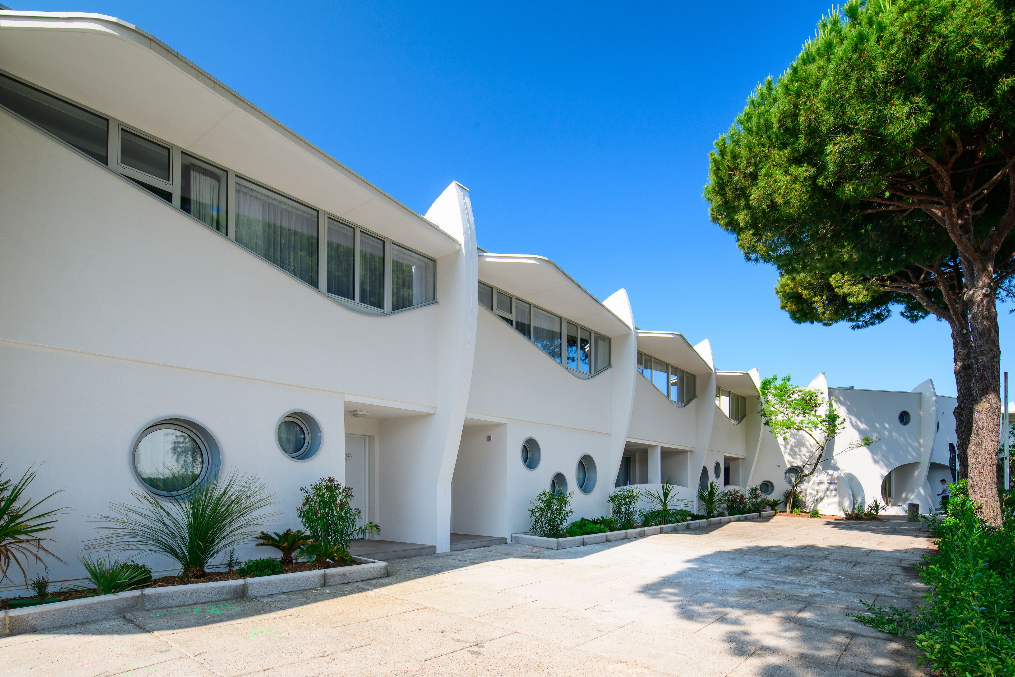 A modern building with a curved facade, large windows, and a paved courtyard with plants.