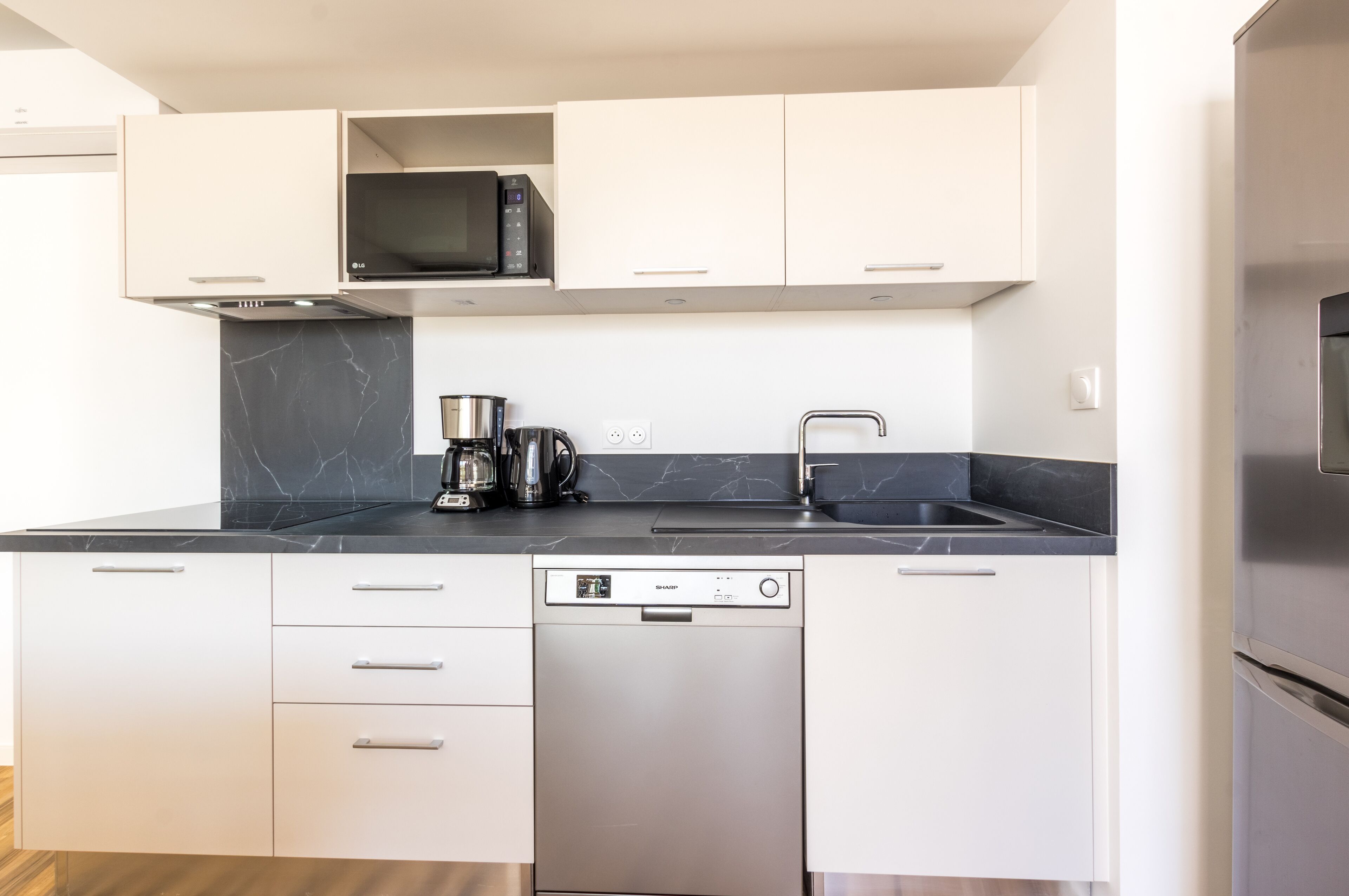 A modern kitchen with white cabinets, a black countertop, a built-in microwave, a coffee maker, and a dishwasher.