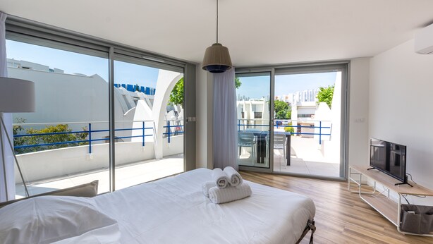 Una camera d'albergo moderna con un letto grande, una TV e un balcone con vista sulla città.