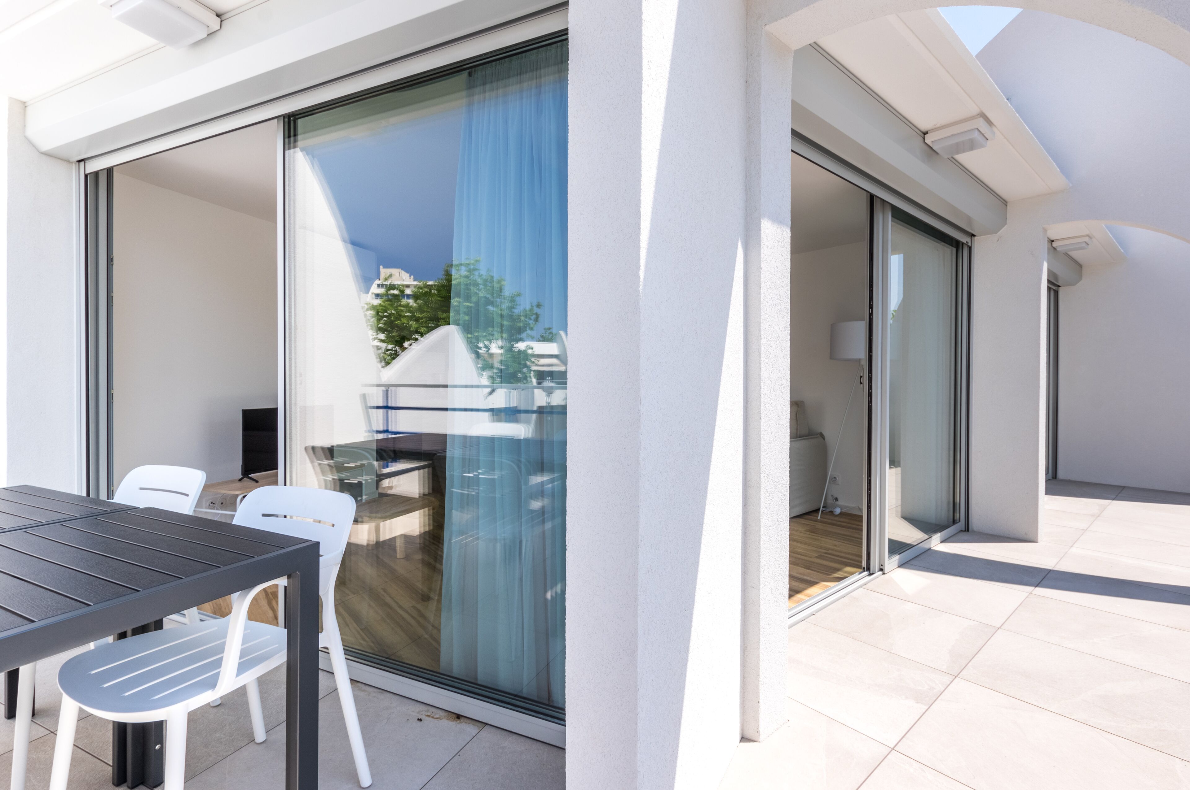 A modern outdoor dining area with a glass sliding door, white chairs, and a black table.