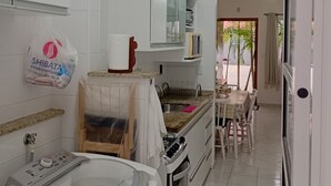 A kitchen with white cabinets, a microwave, a sink, and a dining area with a table and chairs. - Apartamento Térreo, no Local Mais Estratégico de Ubatuba!!! (Ubatuba)