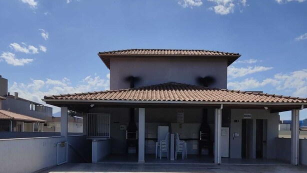 A swimming pool with a tiled deck, a covered seating area, and a building with a tiled roof. - Apartamento Térreo, no Local Mais Estratégico de Ubatuba!!! (Ubatuba)
