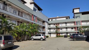 A multi-story building with balconies, parked cars, and palm trees. - Apartamento Térreo, no Local Mais Estratégico de Ubatuba!!! (Ubatuba)