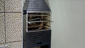A brick-built outdoor oven with a chimney, located in a corner with tiled flooring and a metal rack. - Apartamento Térreo, no Local Mais Estratégico de Ubatuba!!! (Ubatuba)