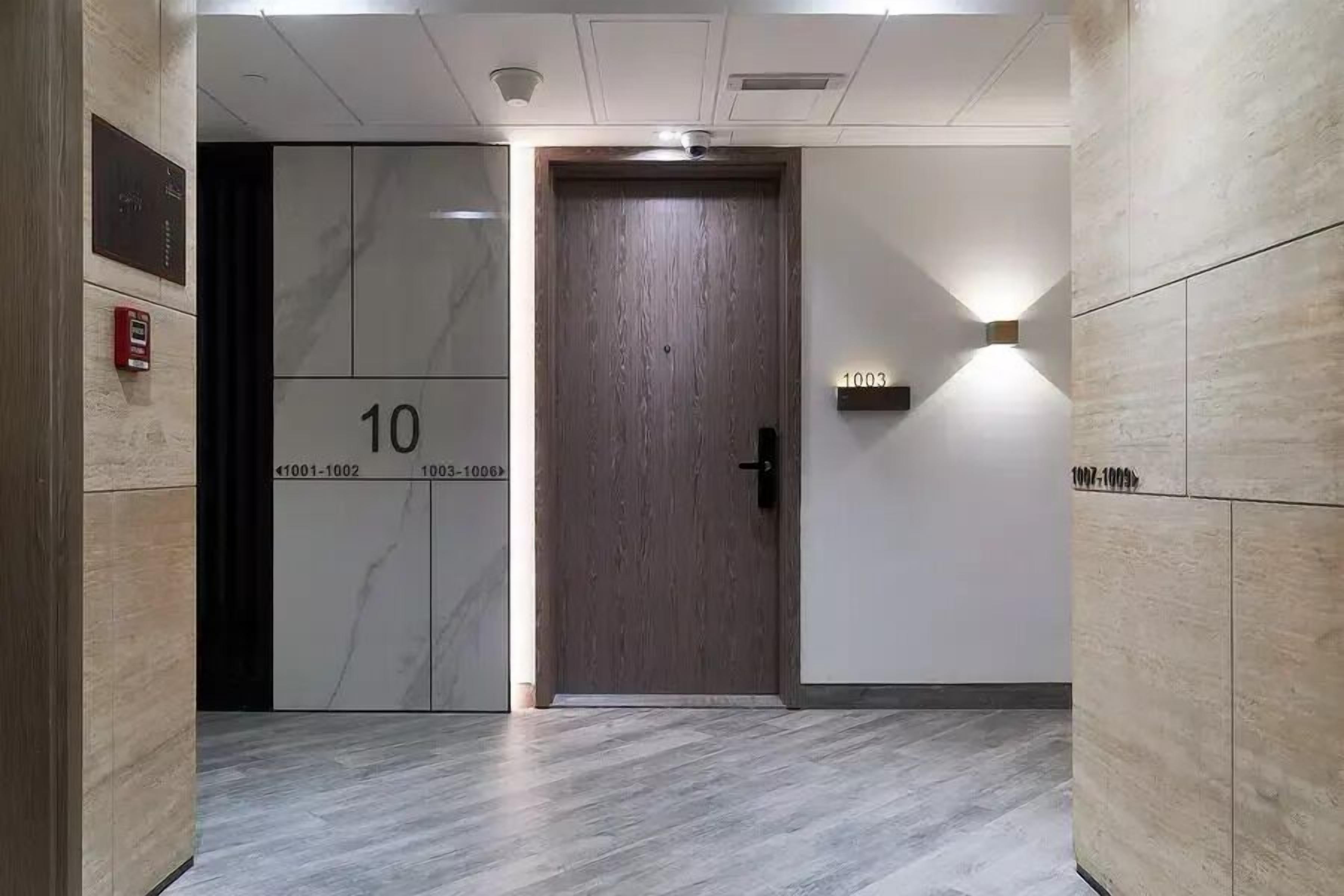 En hall med en dörr av trä, märkt med nummer 10, och en väggmonterad lampa.