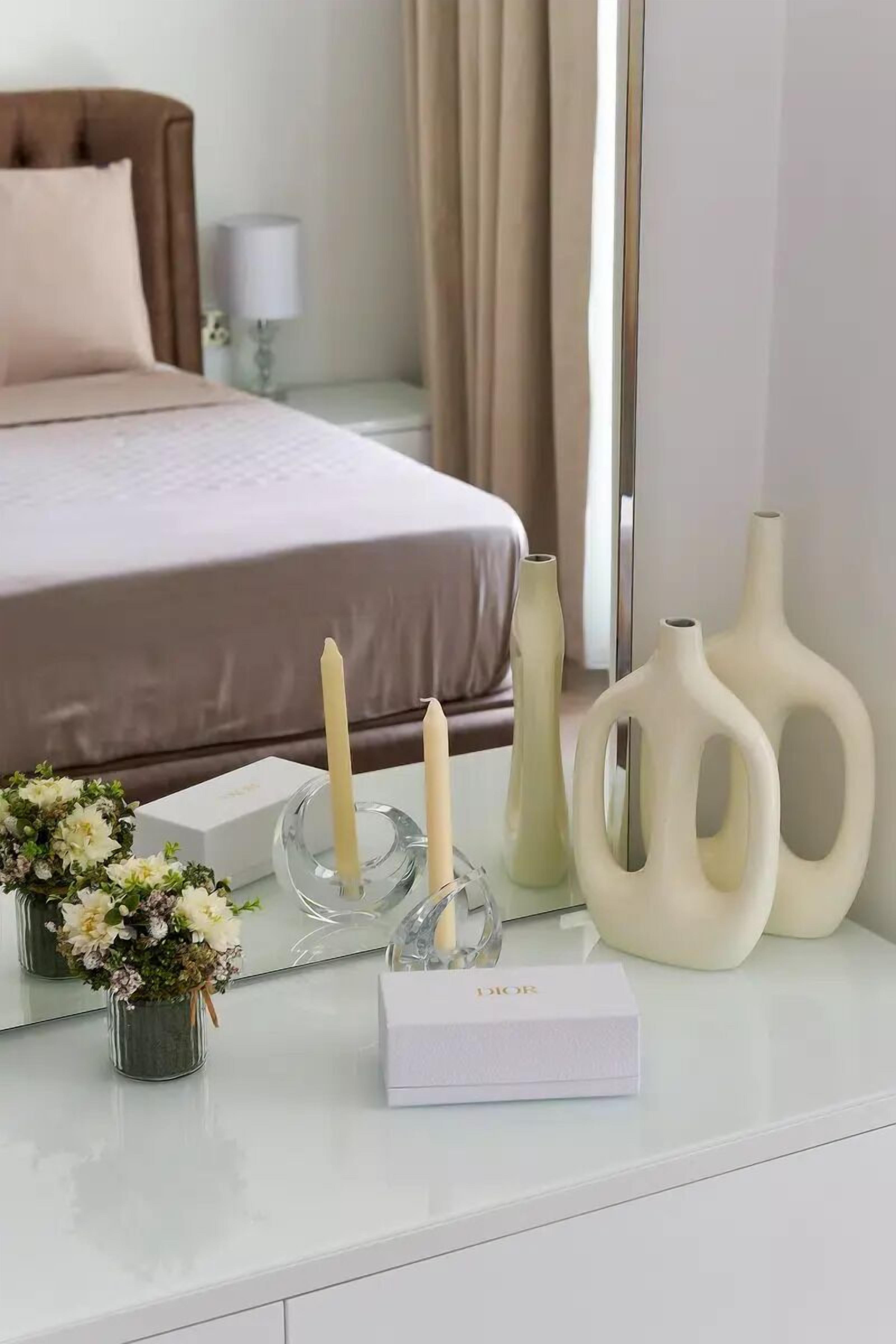 Un dormitorio ordenado con cama, mesita de noche y objetos decorativos, incluyendo velas y jarrones.