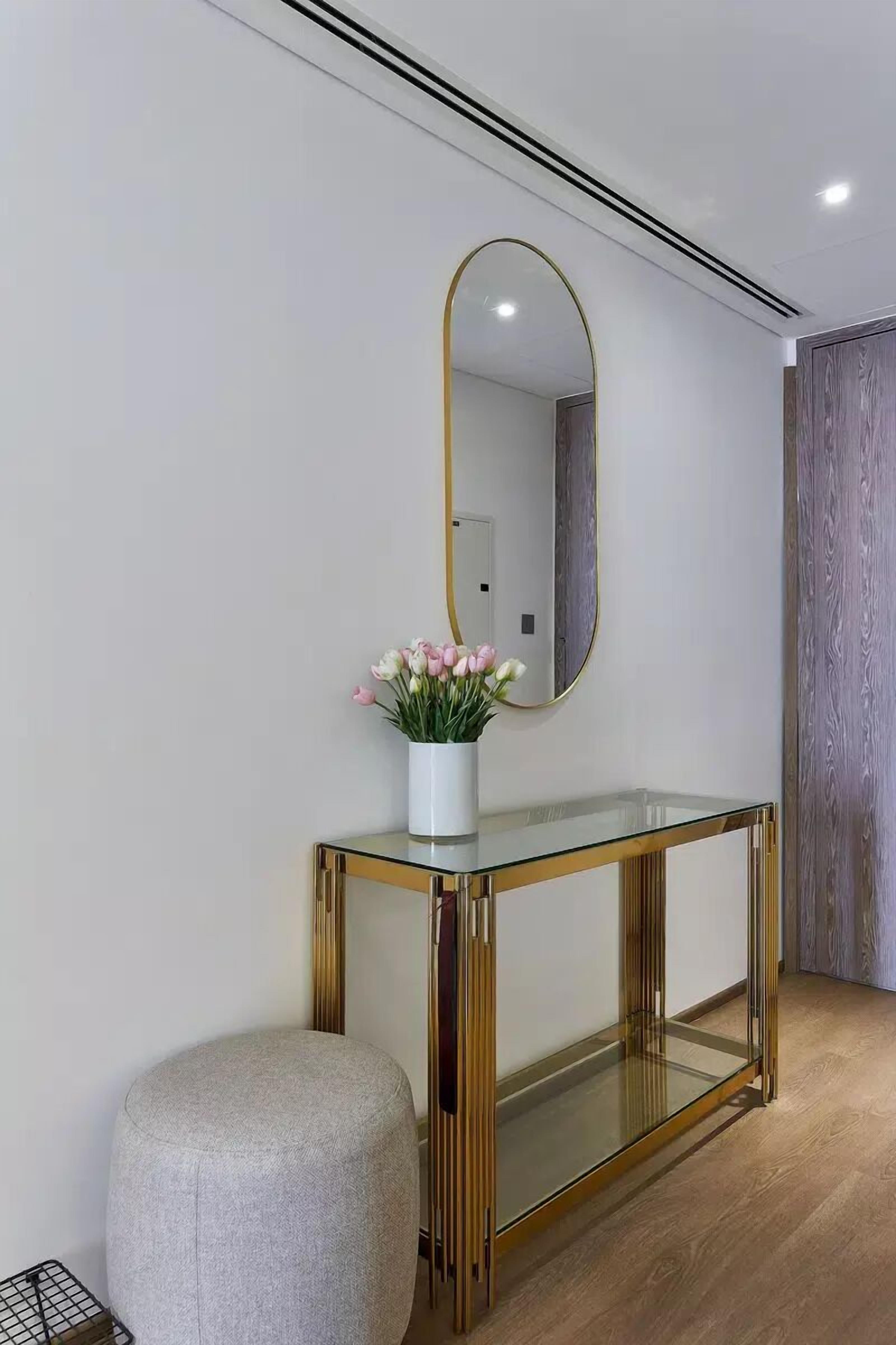 A modern entryway with a glass console table, a gold-framed mirror, and a vase of flowers.