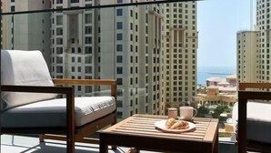 A balcony with a view of high-rise buildings and the sea. There are two chairs and a small table with a plate of croissants and a cup. - New apt in Dubai Marina with balcony (Dubai)
