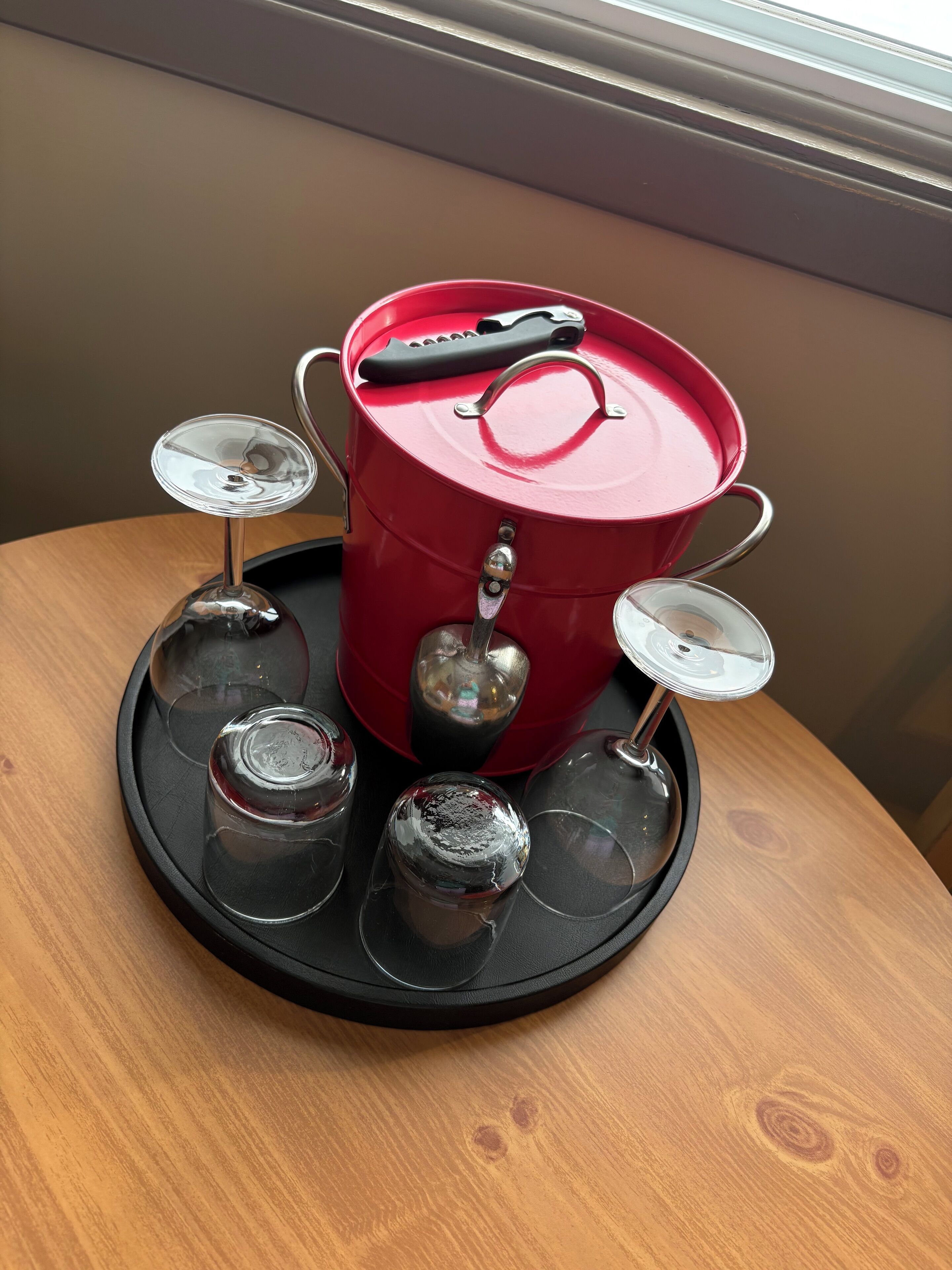 Un pot rouge avec un couvercle et une anse, posé sur un plateau noir, entouré de quatre verres vides.