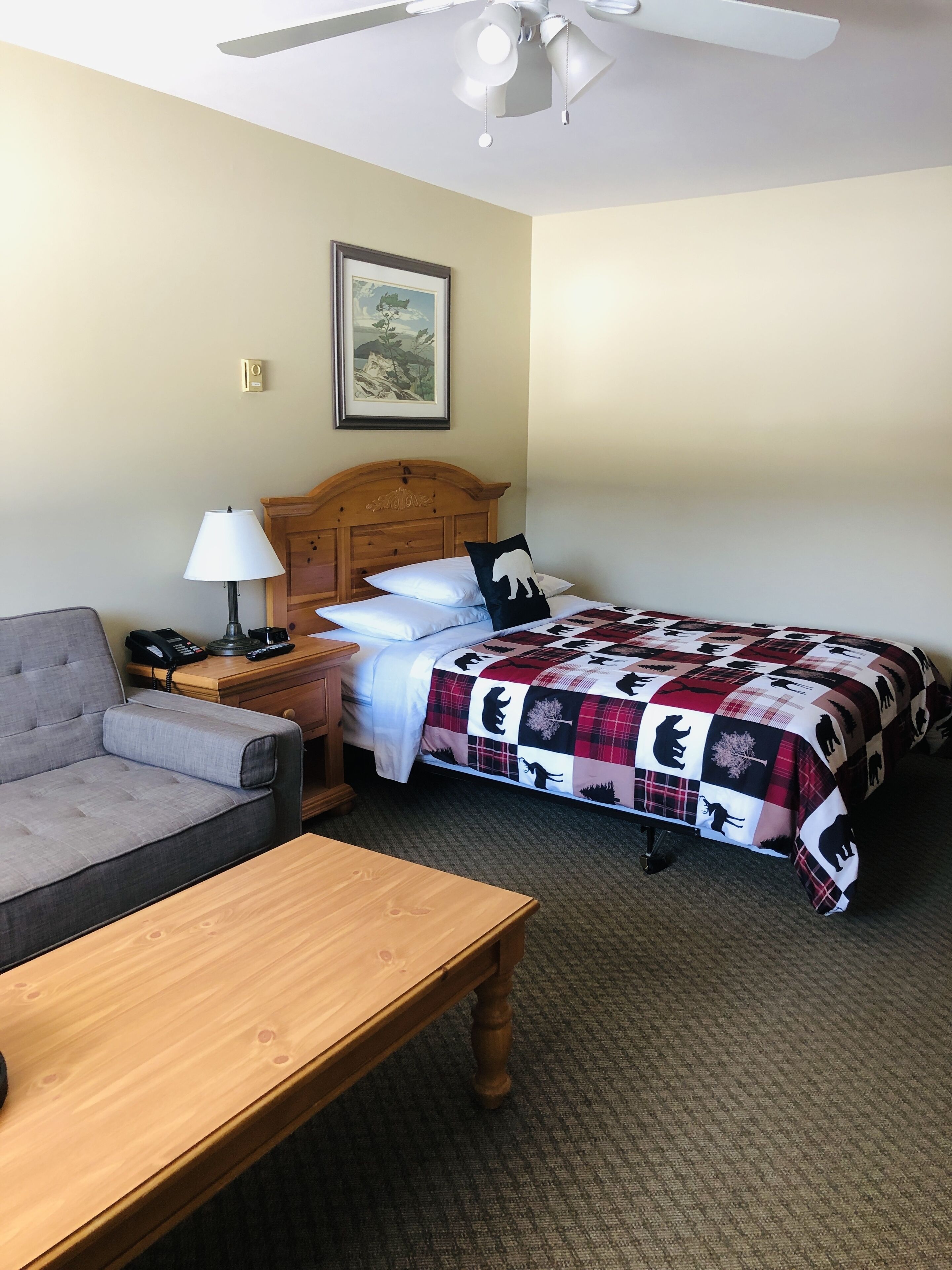 Une chambre d’hôtel comprenant un lit, un canapé, une table en bois, une table de chevet avec une lampe et un ventilateur de plafond.