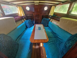 Ein gemütliches Interieur mit einem zentralen Holztisch, blauen Sitzkissen und zwei mit Vorhängen versehenen Fenstern.