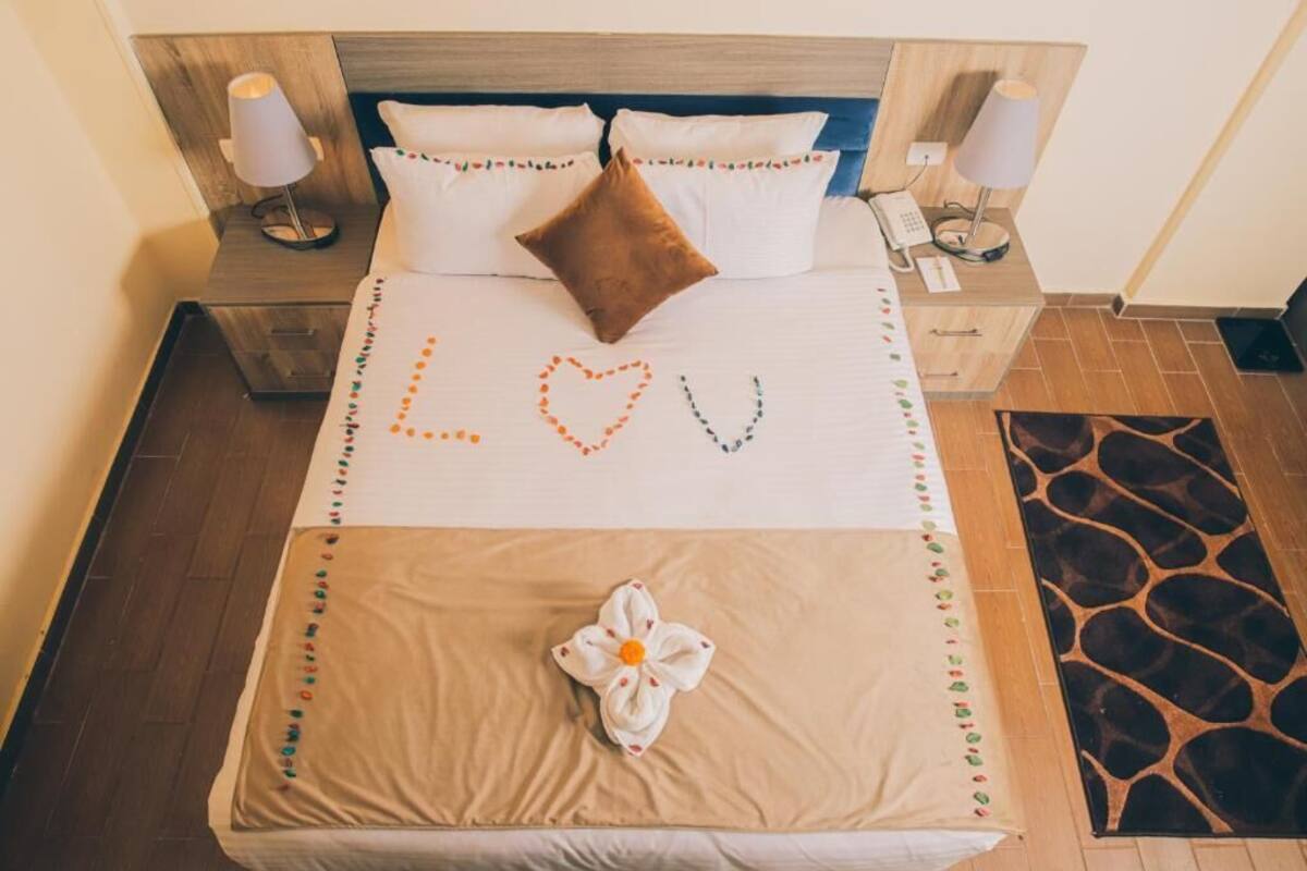 A neatly made bed with a heart-shaped decoration on the bedspread, a brown pillow, and a flower on the bed.