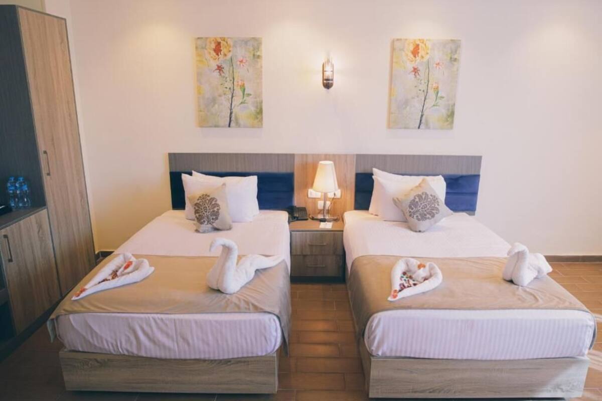 A hotel room with two beds, each with a swan towel, a bedside lamp, and a painting on the wall.