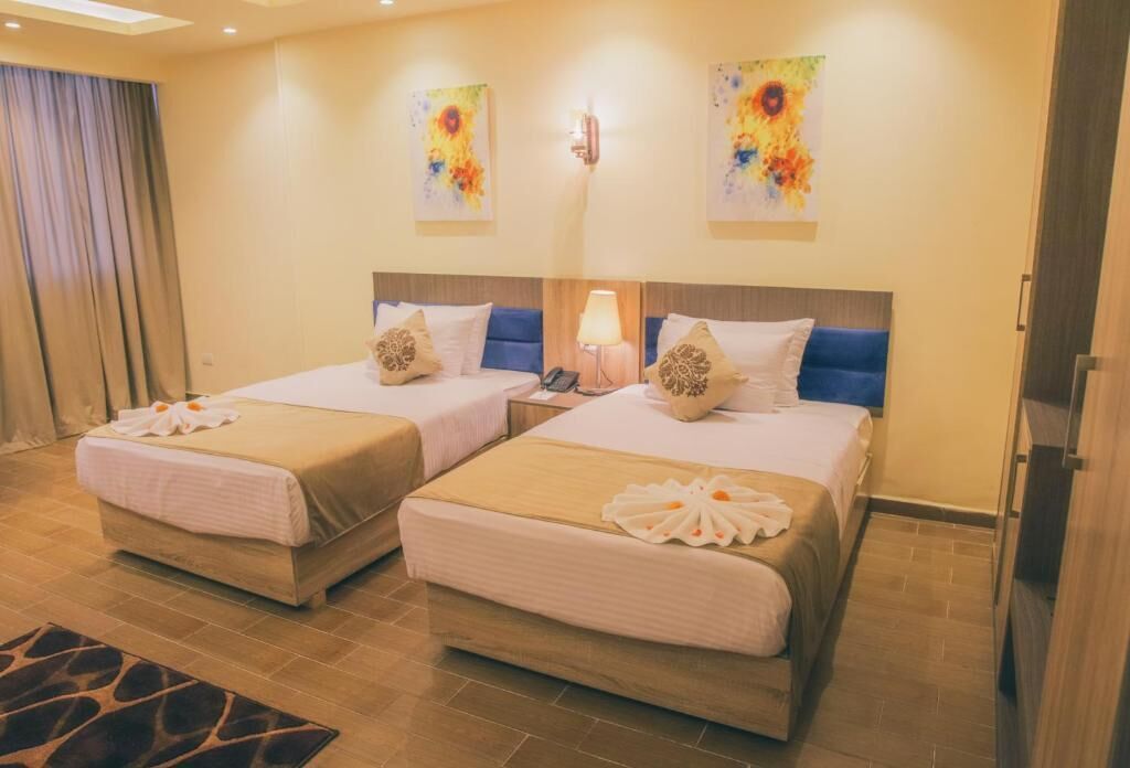A hotel room with two beds, a nightstand, a lamp, and artwork on the walls.