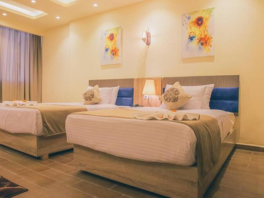 Habitación de hotel con dos camas, un ventanal con cortinas y dos cuadros abstractos en la pared.