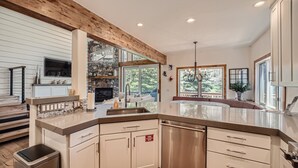 A modern kitchen with white cabinetry, a stainless steel dishwasher, and a stone accent wall. - 1890 Lions Ridge Loop, #9-West Vail Remodeled Home, Hot Tub, On Bus Route, Close to Vail! (Vail)